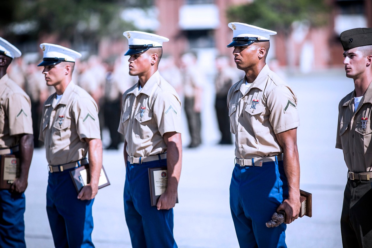 Marines standing at attention while holding awards and certificates.