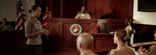 A Marine Judge Advocate presents to other uniformed Marines in a court room.