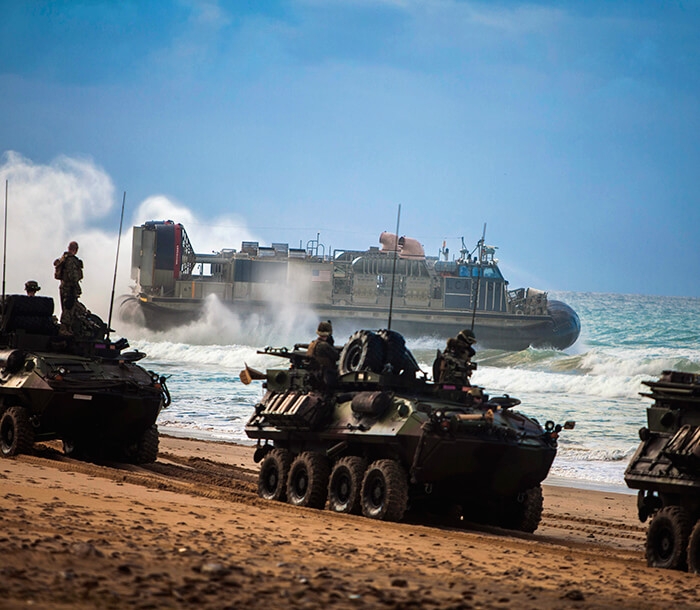 Los Marines in Light Armored Vehicles (LAV) se alinean en una playa de arena.