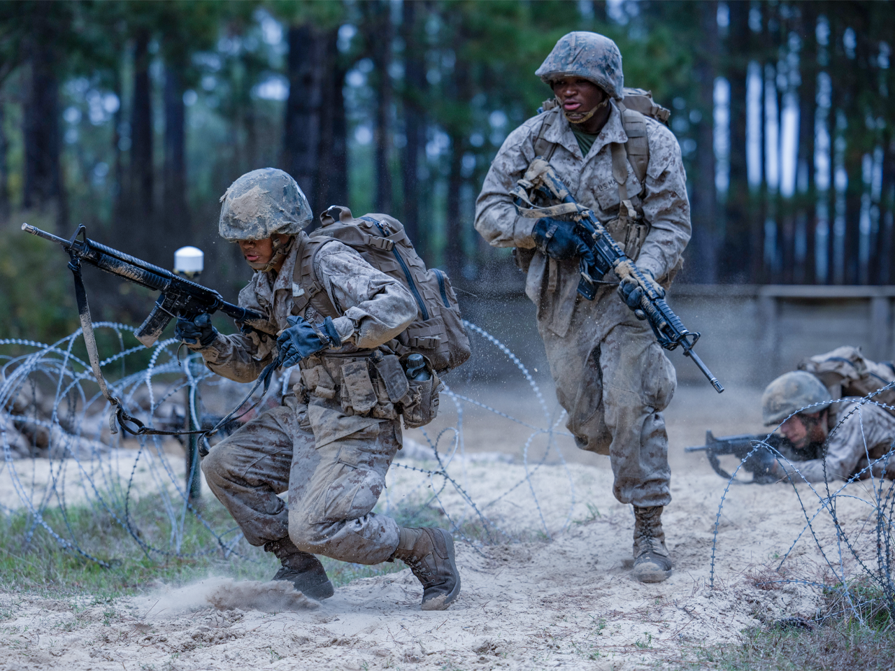 Marines in full combat gear navigating Crucible obstacle course with barbed wire during final training test.