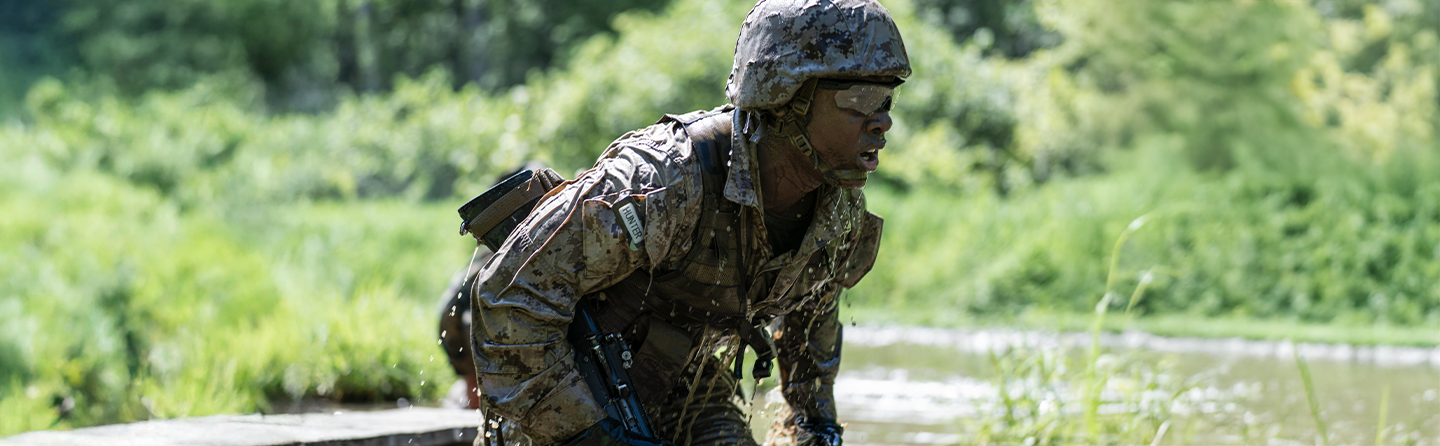 Marine officer candidate covered in mud completes obstacle during combat endurance course at Officer Candidates School.
