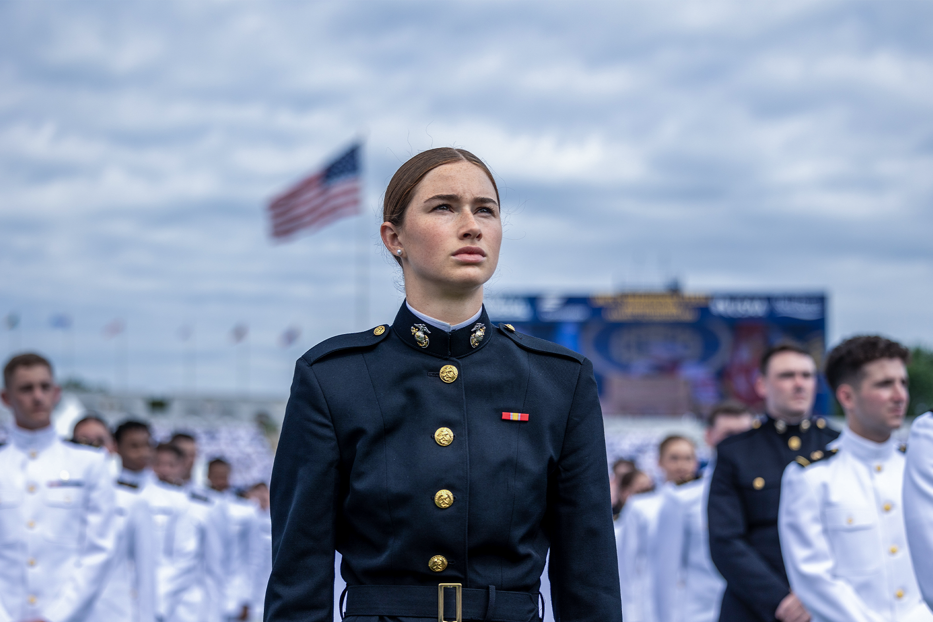 Female Marine officer in dress blue uniform with service ribbons at outdoor military ceremony.