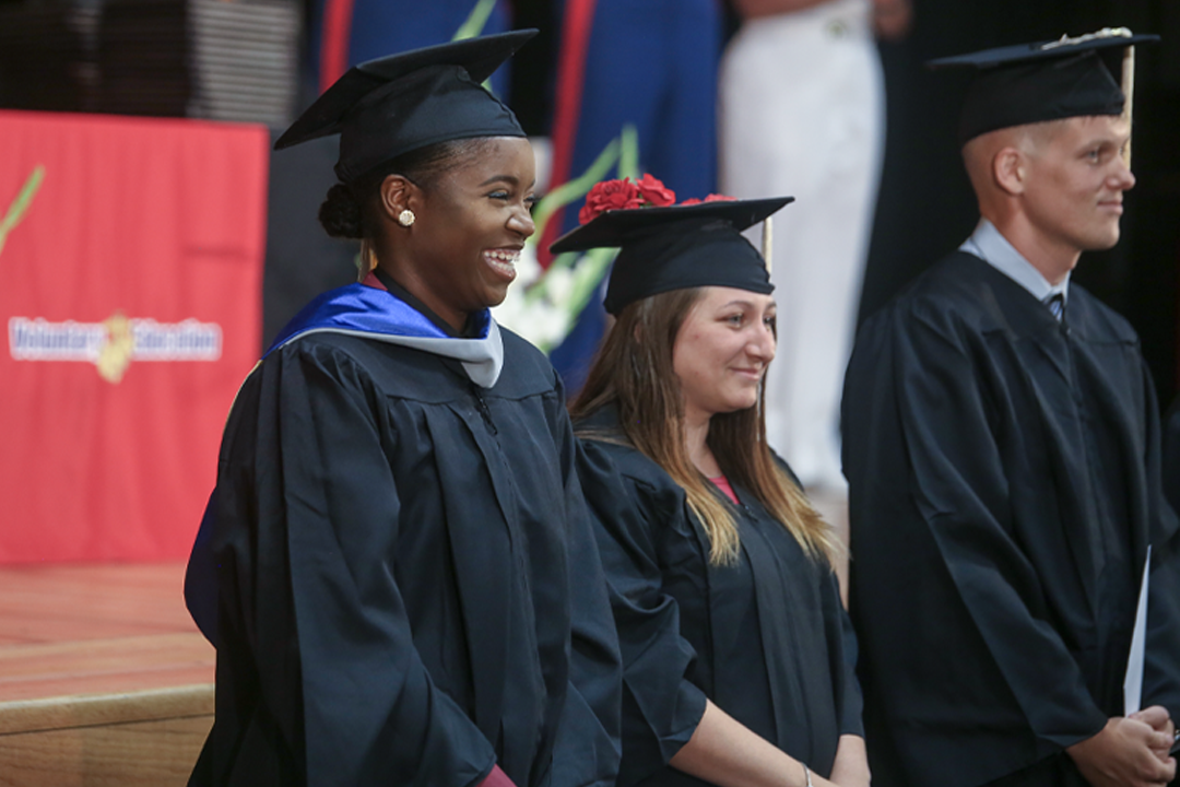 College graduates in black caps and gowns smiling during graduation ceremony commencement.
