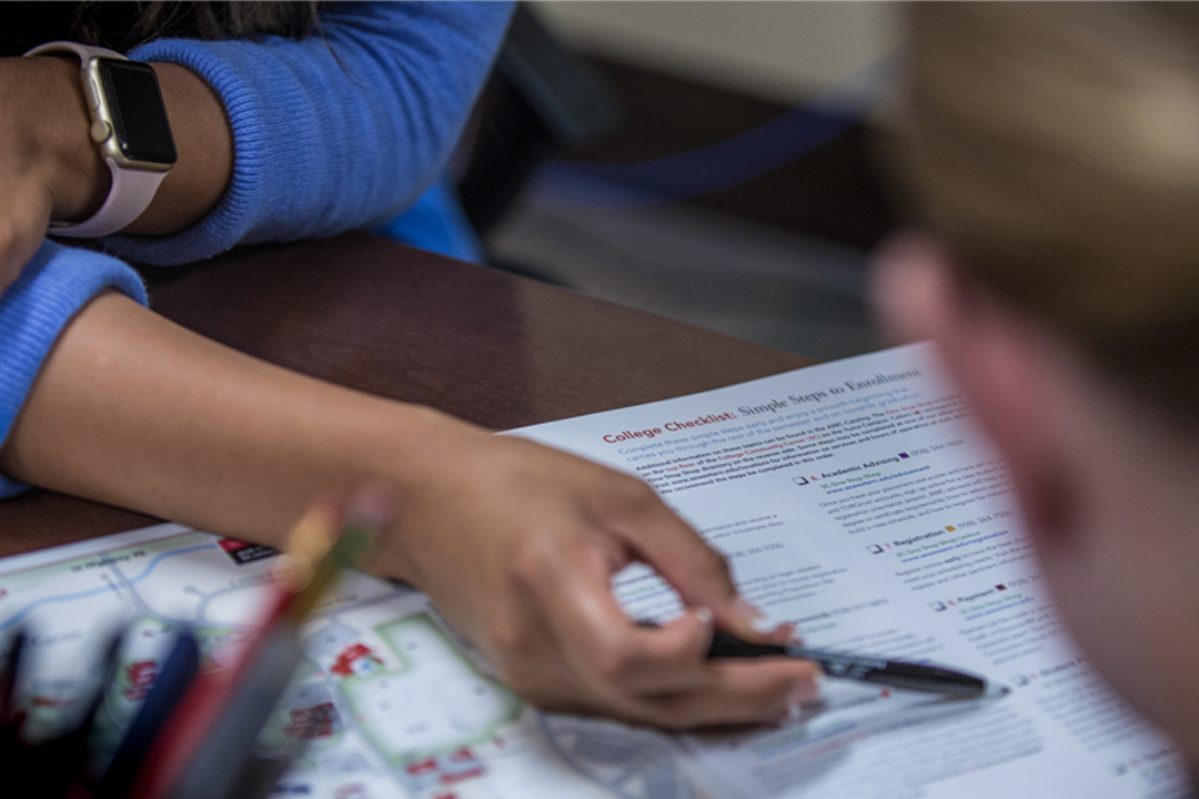 Student reviewing college checklist and education documents at desk with smartphone and materials.