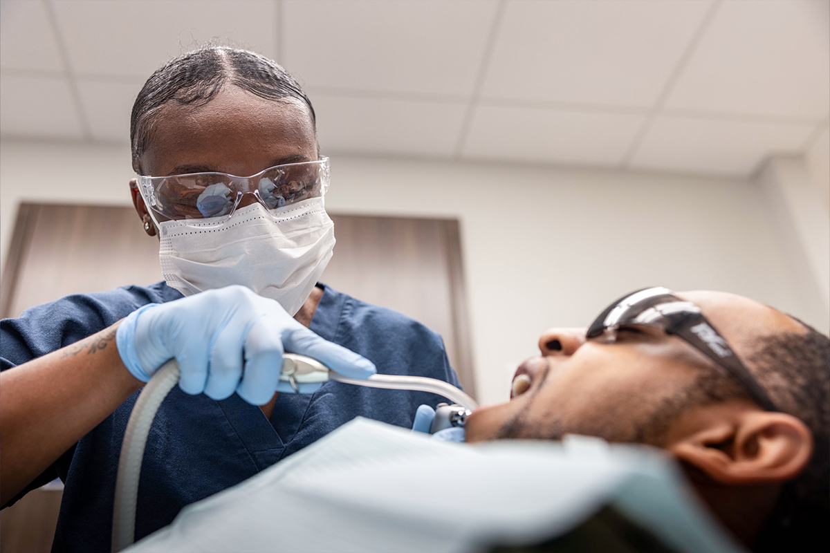 Marines dentist in protective gear performing dental procedure on patient demonstrating comprehensive healthcare coverage benefits.