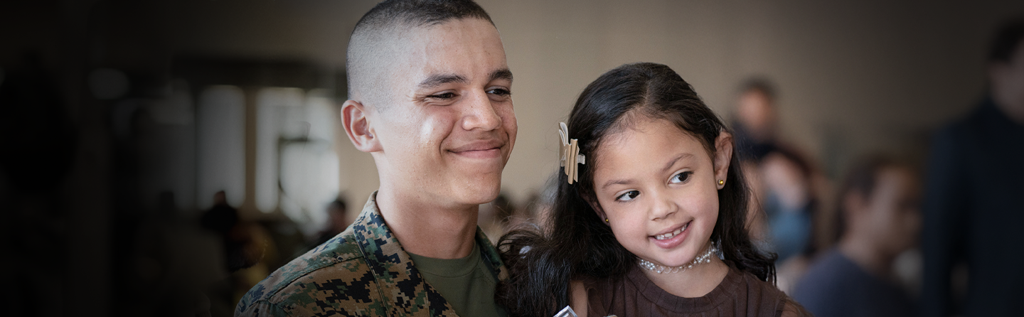 Marine in woodland camouflage smiling with young daughter showcasing family health benefits and support programs.