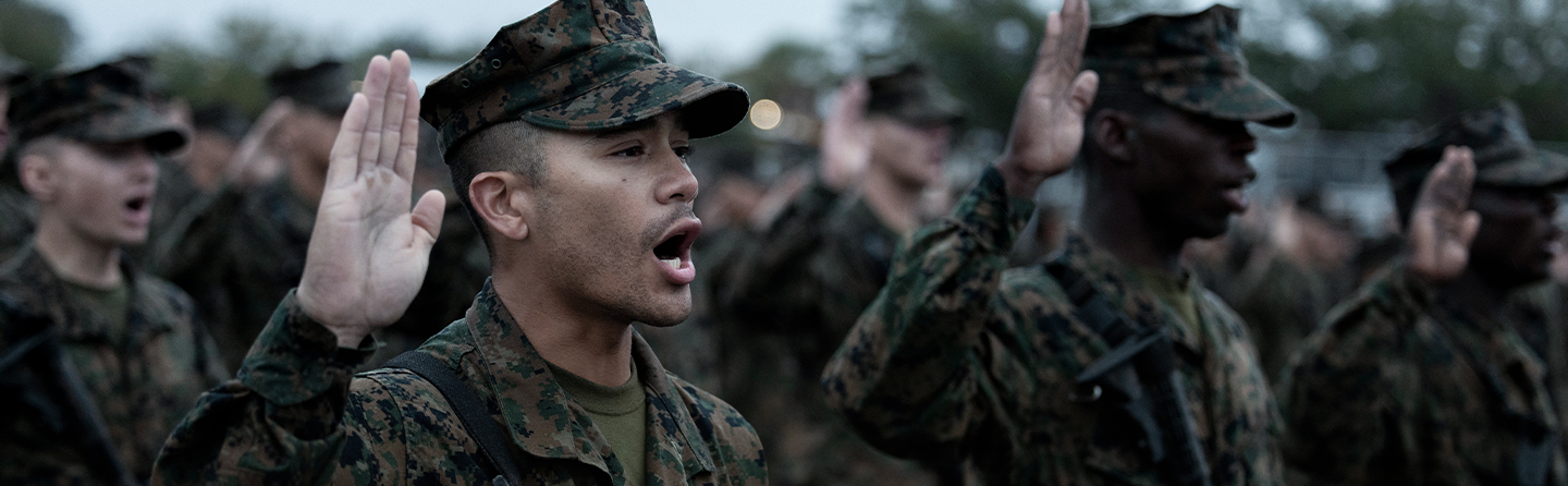 Marine recruits in woodland camouflage with raised hands taking oath during recruit training graduation ceremony.