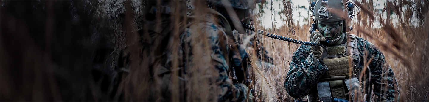 Marines with tactical gear and communications equipment conduct operations in tall grass field at Camp Lejeune.
