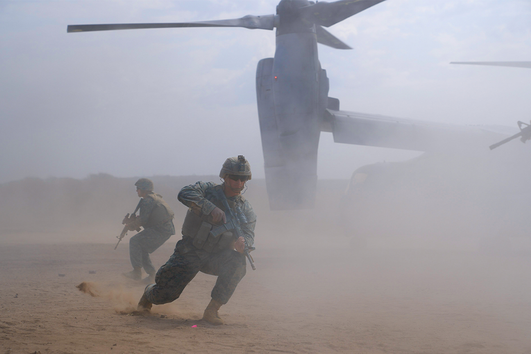 Marines exit V-22 Osprey aircraft during amphibious assault training operation in dusty desert conditions.