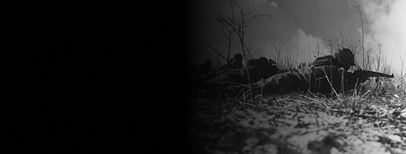 A black and white image of Marines fighting during the battle of Chosin Reservoir. They are on their stomachs, aiming their rifles.