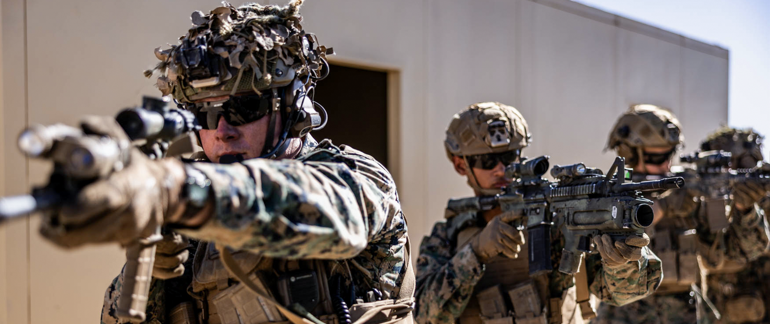 Marines complete a training in a mock combat town in the desert. They look down the scopes of their weapons as they move amongst buildings.