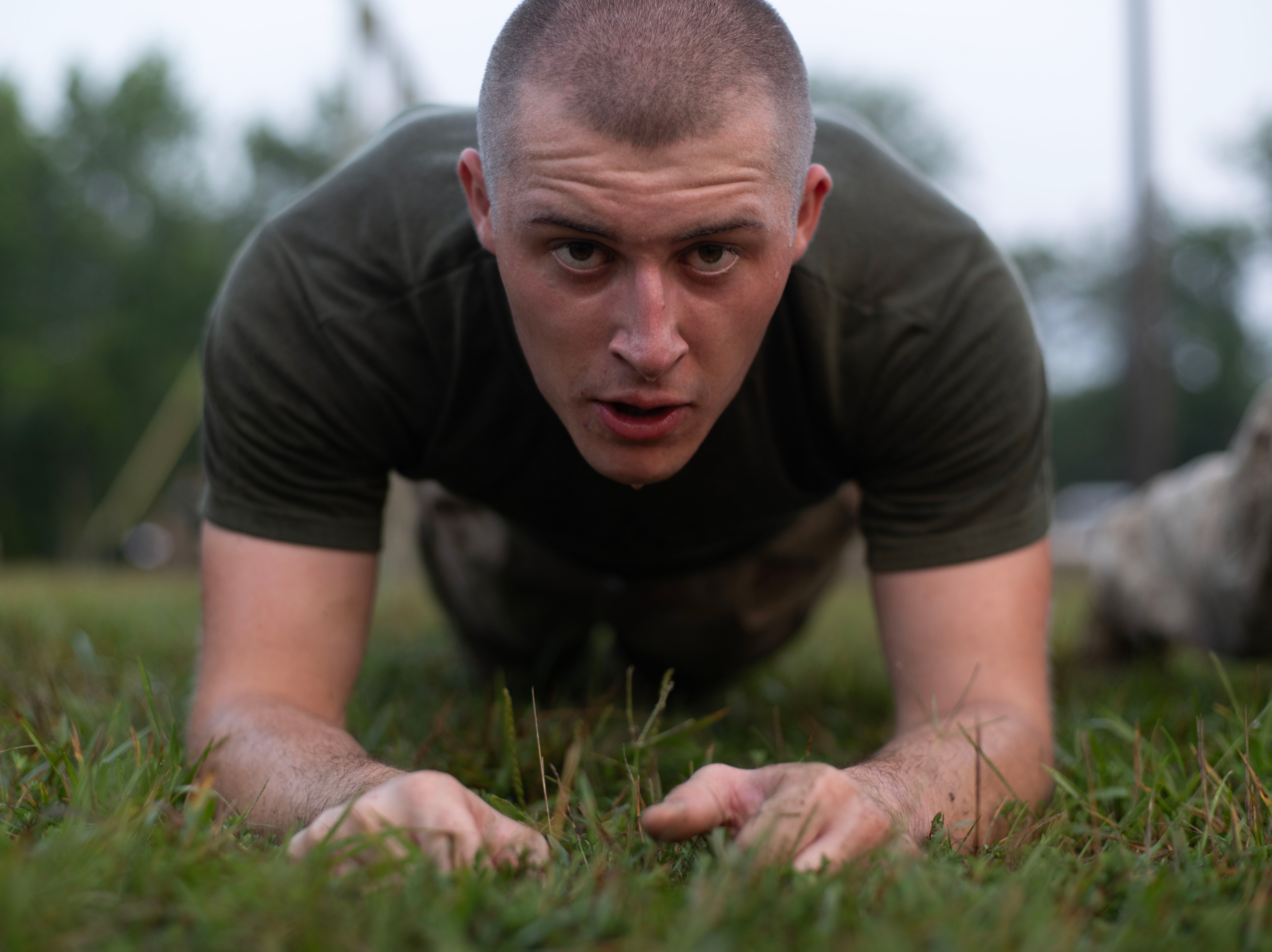  A Marine recruit with a shaved head completes a plank. He is looking straight into camera. 