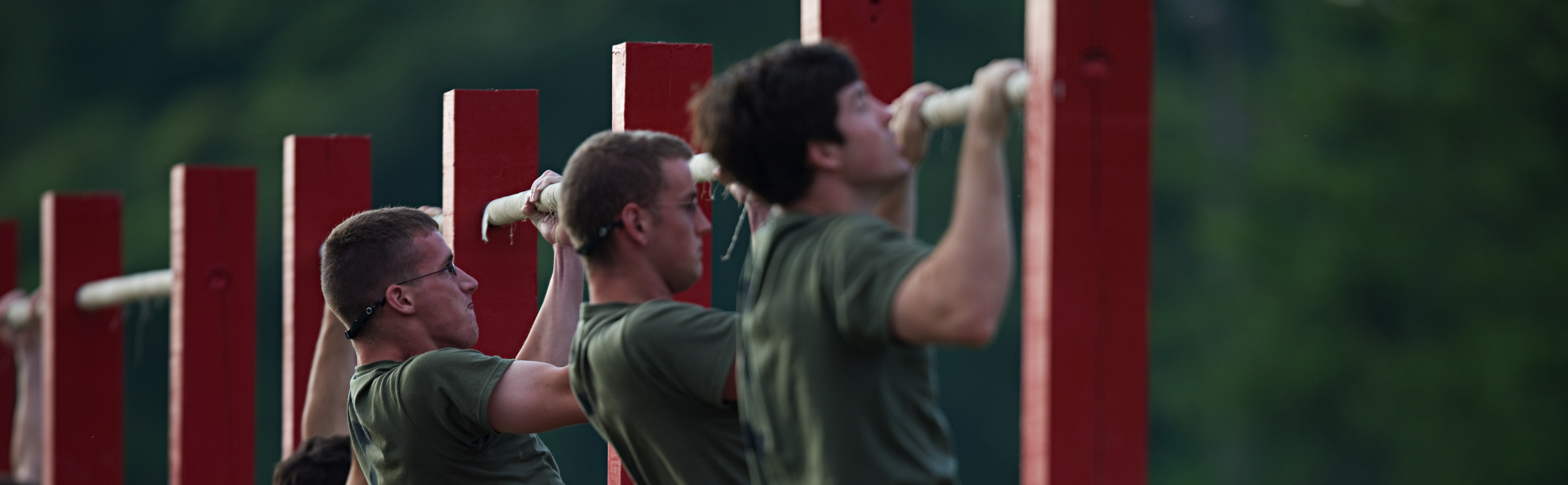 Male Marines complete pull-ups on pull-up bars during the physical fitness test. Other Marines watch them complete the assessment. 