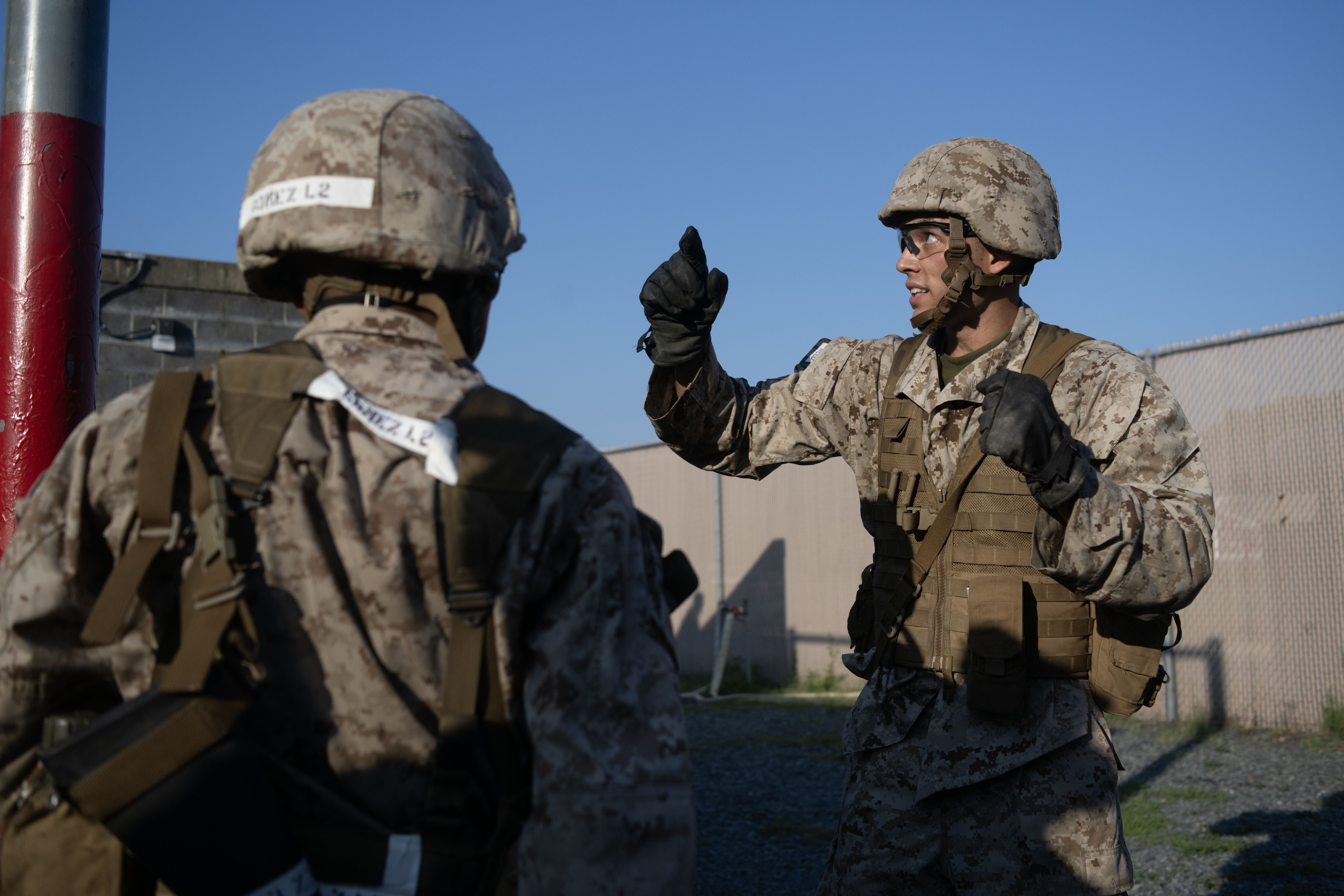 Two Marine officer candidates in camouflage utilities and helmets talk through their approach during a Leadership Reaction Course exercise, one gesturing as he explains.