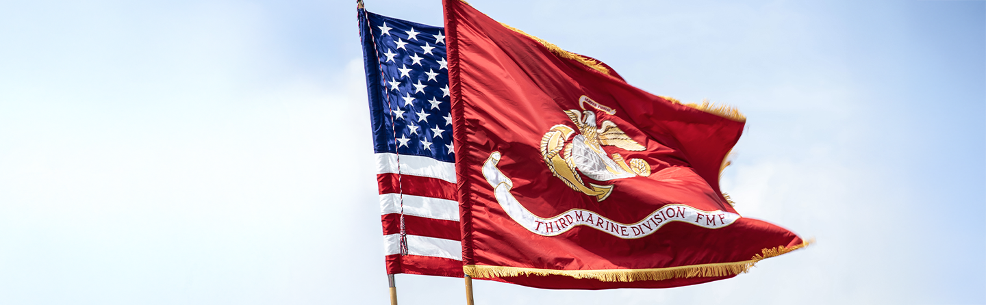 American flag and Marine Corps flag with Eagle Globe and Anchor emblem flying together against clear blue sky.