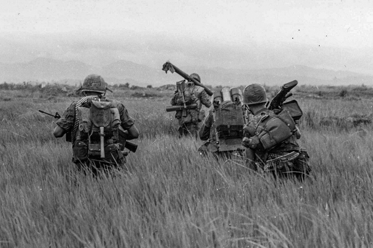 Marines in combat during Battle of Hue with machine guns positioned in tall grass field, Vietnam War.