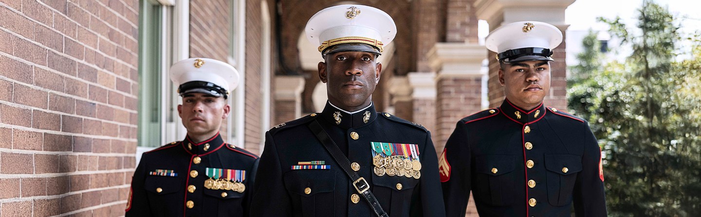 Marines in dress blue uniforms with white covers and ribbons representing honor, courage, and commitment values.