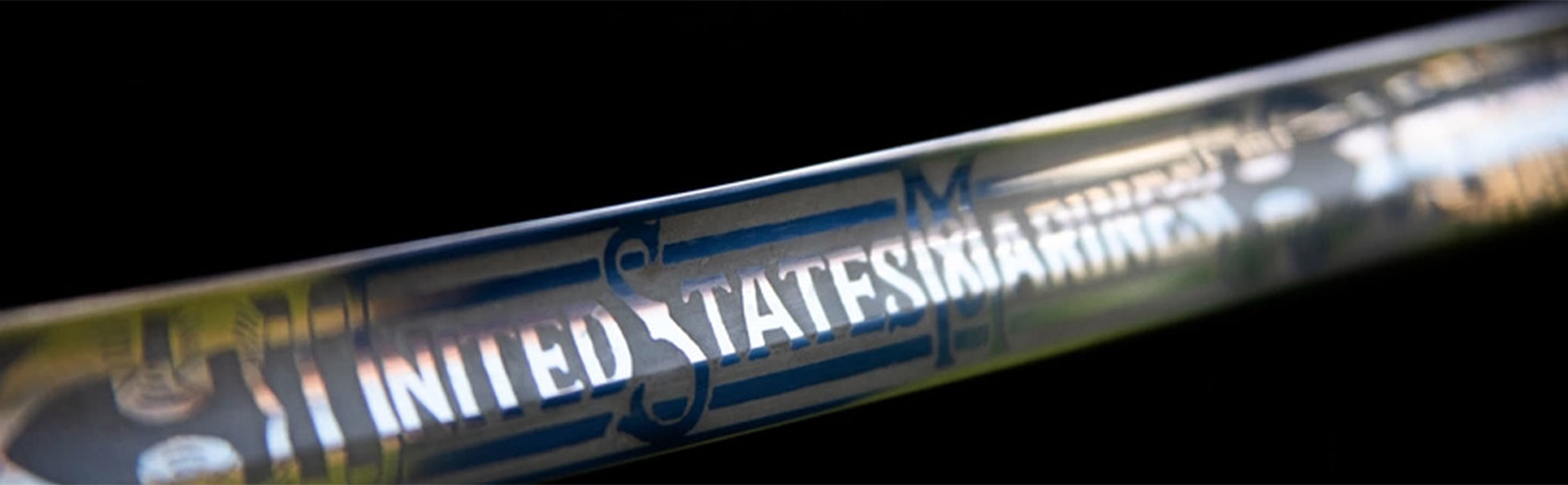 Close-up of a metallic, Mameluke sword with "UNITED STATES MARINES" engraved on it, against a dark background.
