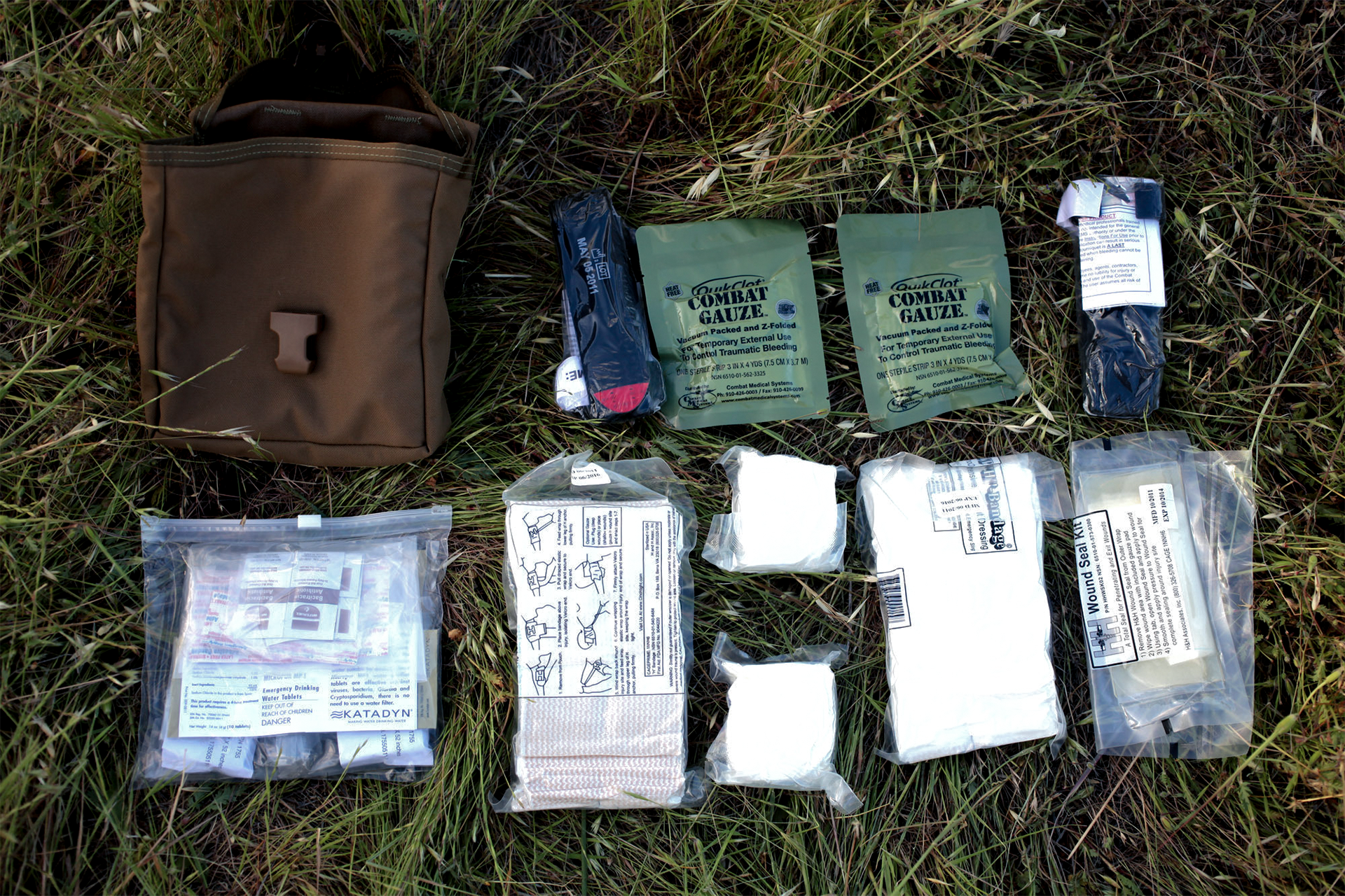 Individual first aid kit contents displayed including combat gauze tourniquets bandages and medical supplies on grass.