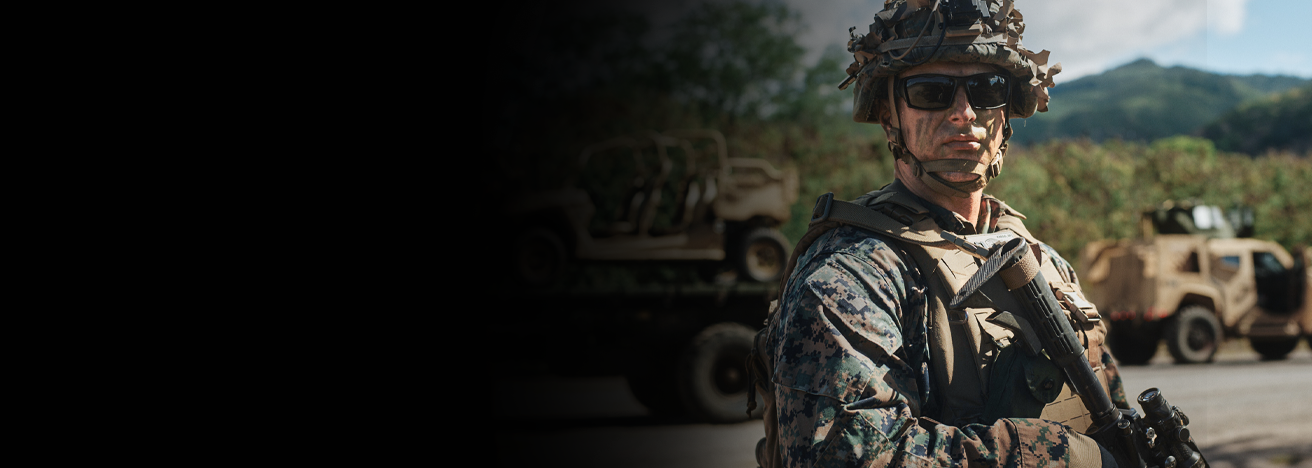Marine in camouflage uniform and tactical gear standing with rifle during field training exercise.