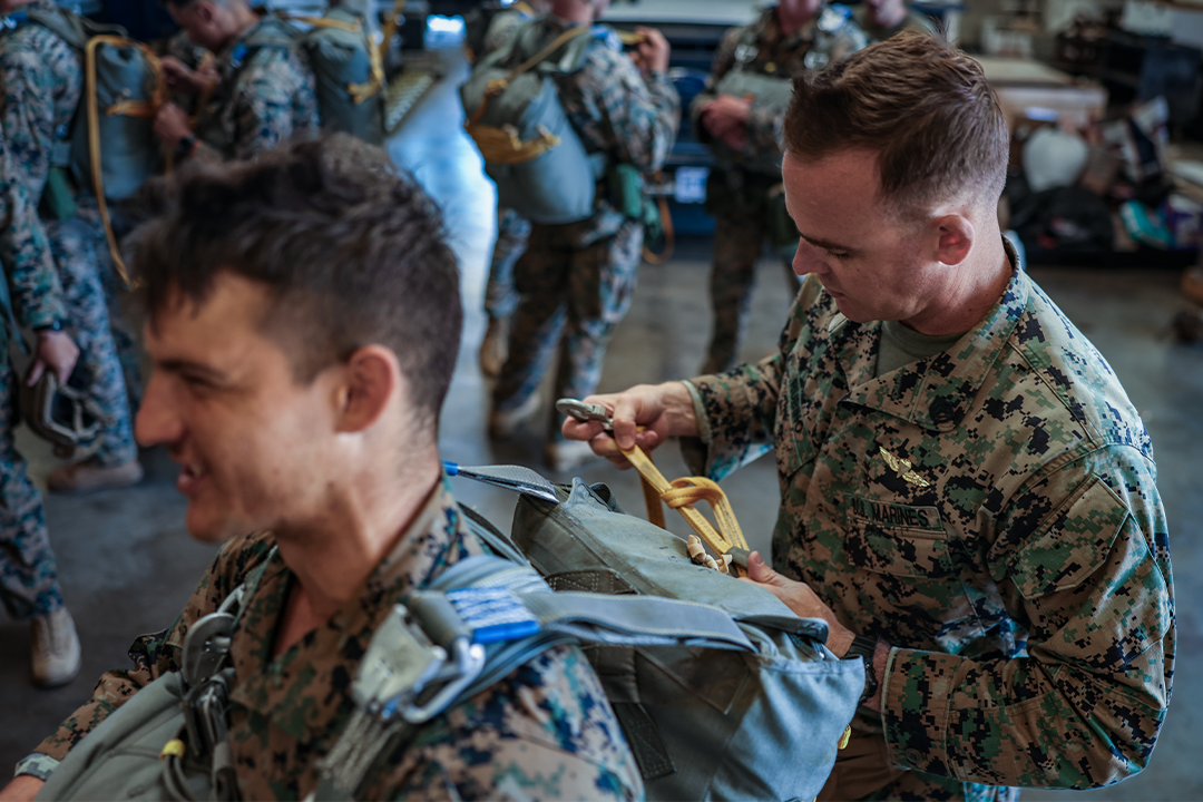 A parachute rigger Marine with a parachutist badge inspects the parachute on the back of another Marine.
