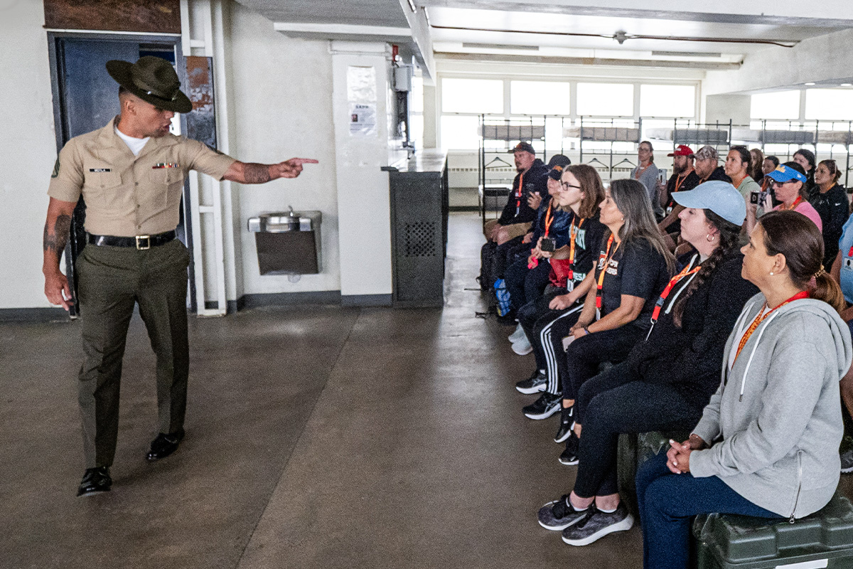 Officer candidate observes team navigate rope obstacle course during leadership training exercise wearing protective gear.