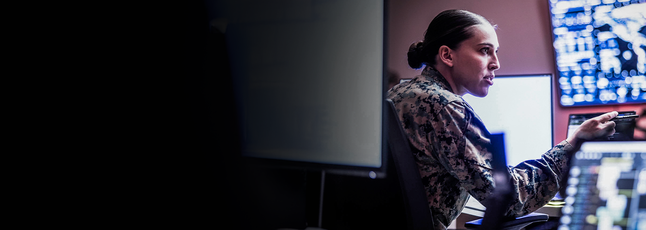 First Lieutenant Annie Parnell points at screen while conducting cyber operations at workstation with multiple monitors.