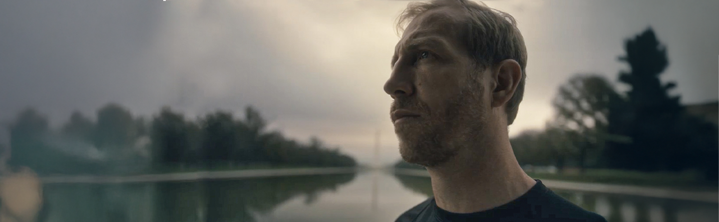 Marine veteran Jake Harriman looks upward outdoors with water and trees in background.