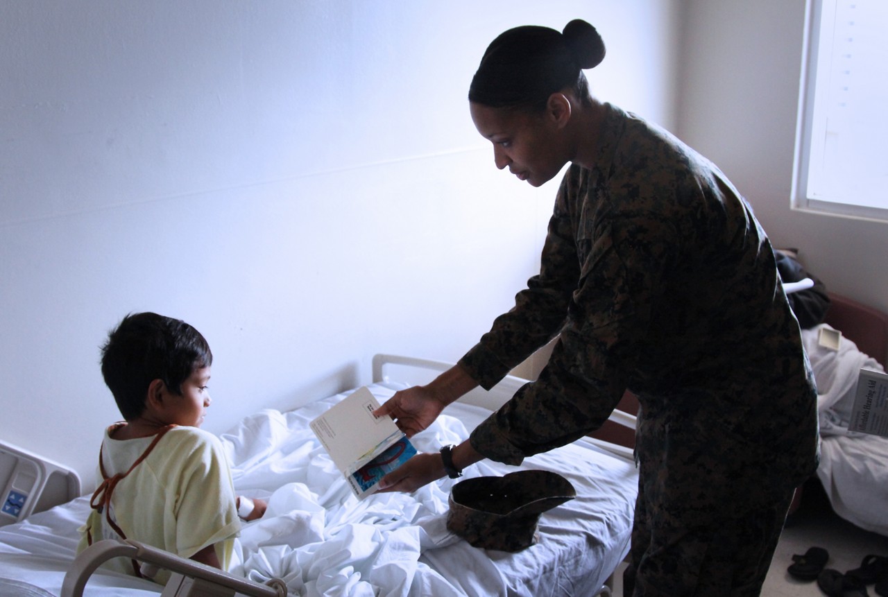 Marine member holding up book for young child in hospital.