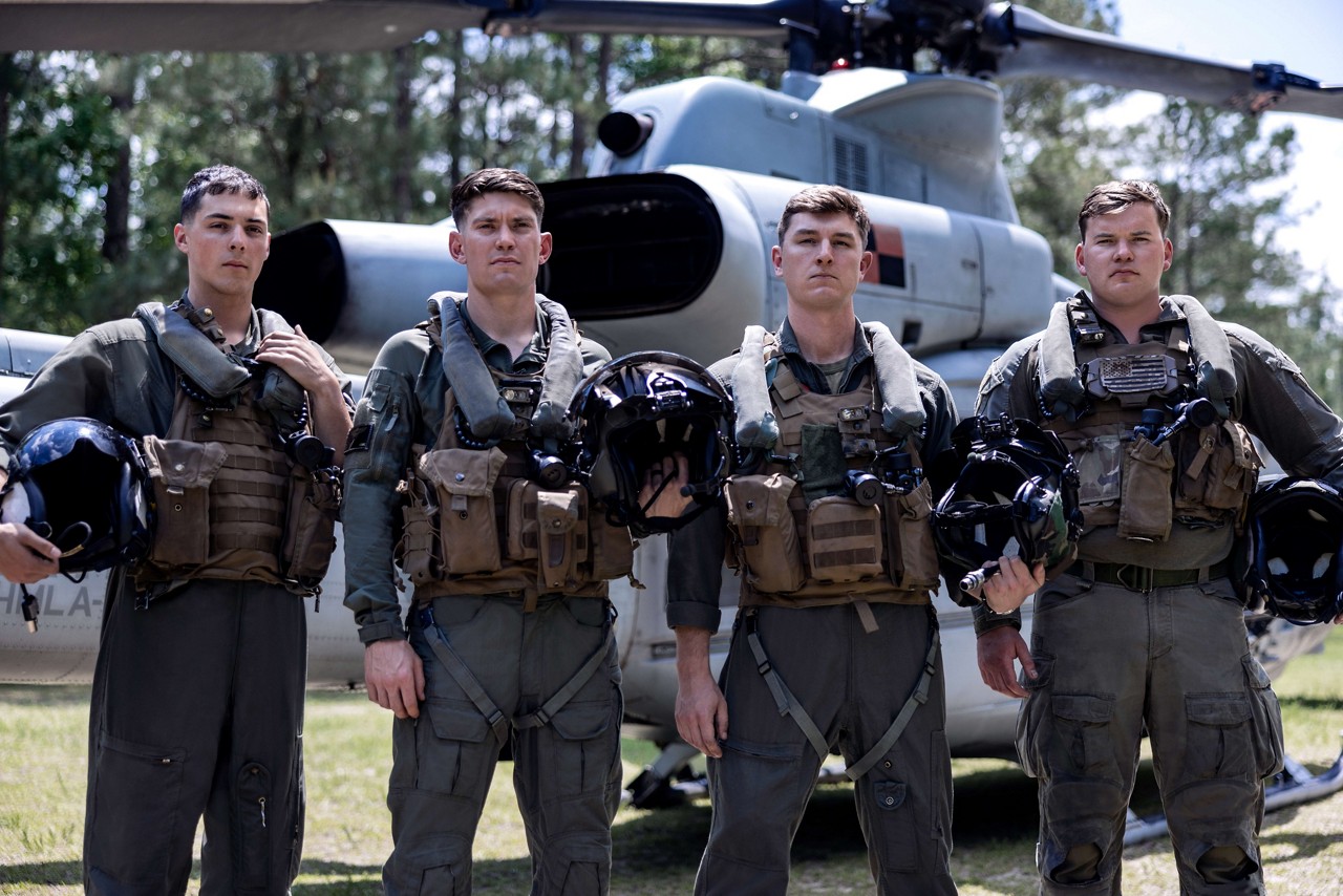Four U.S. Marines in flightsuits hold their helmets in front of a rotor-wing aircraft. 